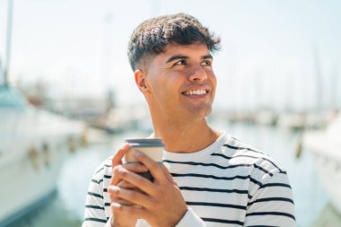 Açık havada elinde kahve tutan ve kuşkuları olan genç İspanyol bir adam.