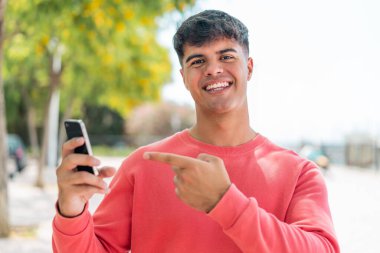 Dışarıdaki İspanyol genç adam cep telefonu kullanıyor ve onu işaret ediyor.