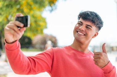 Dışarıdaki İspanyol genç adam cep telefonuyla selfie çekiyor.