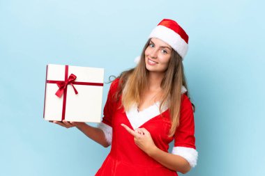 Anne Noel gibi giyinmiş, mavi arka planda izole edilmiş bir hediye taşıyan beyaz bir kadın.