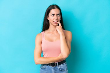 Mavi arka planda izole edilmiş genç beyaz kadın gergin ve korkmuş.