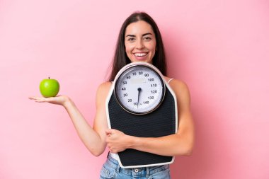 Pembe arka planda, tartı makinesi ve elmasıyla izole edilmiş beyaz bir kadın.