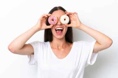 Beyaz arka planda gözünün içinde donut tutan beyaz tenli bir kadın.