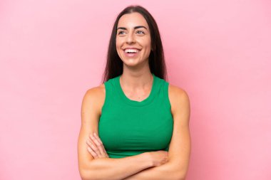 Pembe arka planda izole edilmiş genç beyaz kadın kollarını ön cephede çapraz tutuyor.