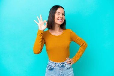 Mavi arka planda izole edilmiş beyaz bir kadın parmaklarıyla tamam işareti gösteriyor.