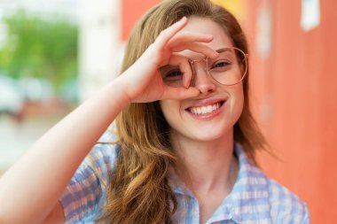 Genç, kızıl saçlı, açık havada, mutlu yüzlü gözlüklü bir kadın.