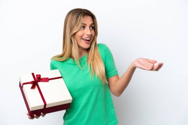 Genç Uruguaylı bir kadın beyaz arka planda sürpriz bir yüz ifadesiyle izole edilmiş bir hediye tutuyor.