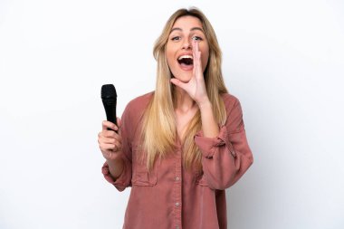 Şarkıcı Uruguaylı kadın beyaz arka planda izole edilmiş bir mikrofonu kaldırıyor ve ağzı açık bağırıyor.