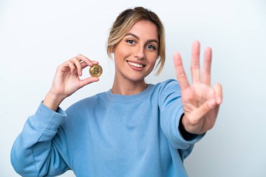Beyaz arka planda Bitcoin tutan genç Uruguaylı kadın mutlu ve parmaklarıyla üçe kadar sayıyor.