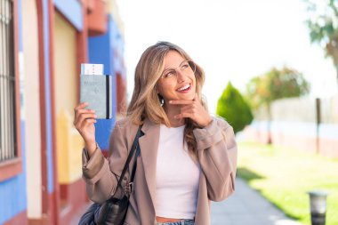 Güzel sarışın Uruguaylı kadın elinde pasaportuyla dışarıda bir fikir üretiyor ve bakıyor.