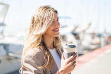 Sarışın, güzel, Uruguaylı bir kadın açık havada elinde mutlu bir ifadeyle kahveyle bekliyor.