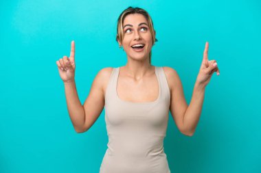 Mavi arka planda izole edilmiş genç beyaz kadın şaşırmış ve yukarı bakıyor.