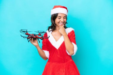 Anne Noel gibi giyinmiş genç bir kadın mavi arka planda izole edilmiş bir dron tutuyor. Yan tarafa bakıyor ve gülümsüyor.