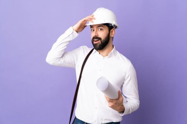 Miğferli genç bir mimar. Mor arka plan üzerinde planlar tutuyor. Yan tarafa bakarken sürpriz jest yapıyor.