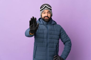 Mor arka planda snowboard gözlüklü kayakçı durdurma hareketi yapıyor.