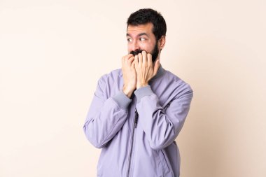 Sakallı beyaz bir adam izole edilmiş arka planda ceket giyiyor gergin ve elleri ağıza vermeye korkuyor.