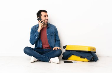 Beyaz tenli yakışıklı bir adam bavul dolusu kıyafetle içeride oturmuş cep telefonuyla sohbet ediyor.