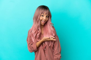 Mavi arka planda izole edilmiş pembe saçlı melez bir kadın gülümseyerek bir fikir sunuyor.