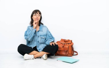 Genç bir kız öğrenci, beyaz arka planda tek başına oturmuş yukarı bakarken bir fikir düşünüyor.