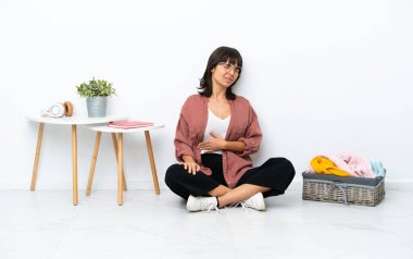 Genç ırk katlayan kadın, beyaz arka planda soyutlanmış bir şekilde yerde oturuyor ve çabaladığı için sırt ağrısı çekiyor.