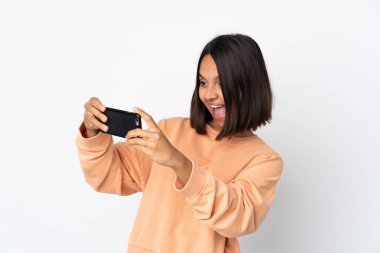 Beyaz arka planda izole edilmiş genç Latin kadın cep telefonuyla oynuyor.