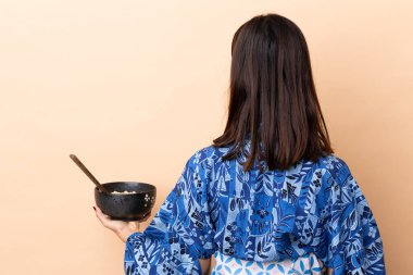 Kadın kimono giyiyor ve elinde yemek çubuklarıyla bir kase erişte tutarken elinde bir kase erişte tutuyor.