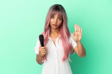 Pembe saçlı, yeşil arka planda izole edilmiş genç, melez bir kadın jest yapıyor.