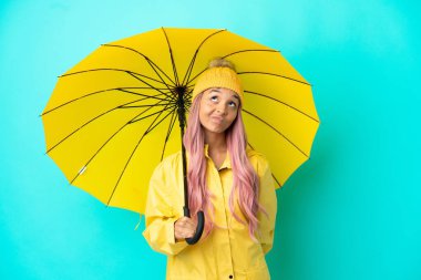 Yağmura dayanıklı paltosu ve şemsiyesi olan genç melez bir kadın.