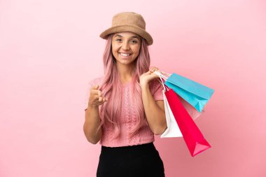 Pembe arka planda izole edilmiş alışveriş çantasıyla genç melez bir kadın iyi bir anlaşma için el sıkışıyor.