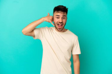 Mavi arka planda izole edilmiş genç beyaz bir adam telefon jesti yapıyor. Bana geri dönüş işareti ver.