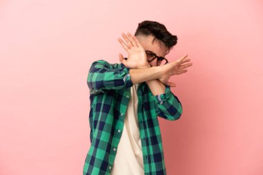 Pembe arka planda izole edilmiş genç beyaz adam sinirden ellerini öne uzatıyor.