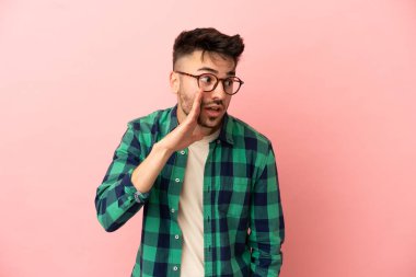 Pembe arka planda izole edilmiş genç beyaz adam yan tarafa bakarken sürpriz bir jest yapıyor.