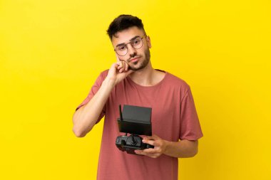 Uzaktan kumandayı elinde tutan adam sarı arka planda izole edilmiş bir fikir düşünüyor.