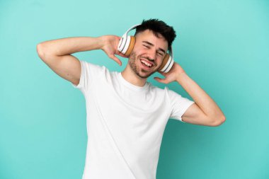 Genç beyaz adam mavi arka planda izole edilmiş müzik dinliyor.