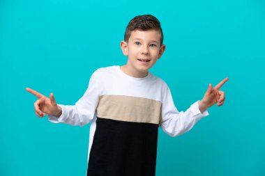 Küçük çocuk mavi arka planda izole edilmiş, parmak uçlarını işaret ediyor ve mutlu.