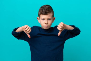 Mavi arka planda izole edilmiş küçük bir çocuk baş parmağını iki eliyle aşağı gösteriyor.