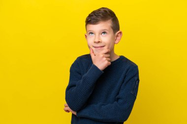 Küçük beyaz çocuk sarı arka planda izole edilmiş bir şekilde yukarı bakarken bir fikir düşünüyor.