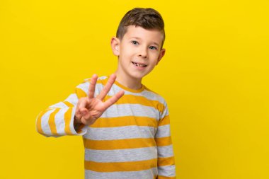 Sarı arka planda izole edilmiş küçük beyaz çocuk mutlu ve parmaklarıyla üçe kadar sayıyor.