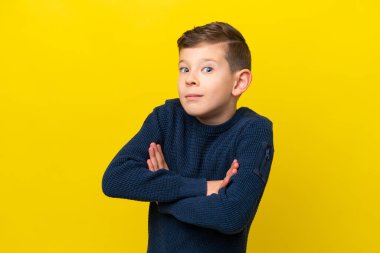 Küçük beyaz çocuk sarı arka planda izole edilmiş. Omuzlarını kaldırırken şüpheyle hareket ediyor.