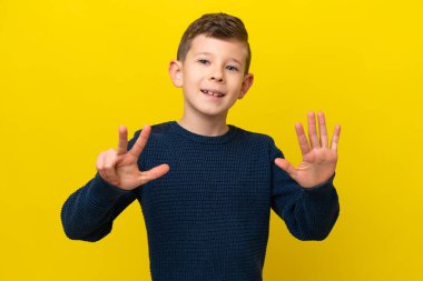 Sarı arka planda izole edilmiş küçük beyaz çocuk parmaklarıyla sekizi sayıyor.