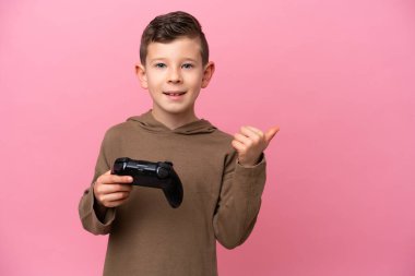 Pembe arka planda izole edilmiş bir bilgisayar oyunu kontrolörüyle oynayan beyaz çocuk bir ürünü sunmak için kenarı işaret ediyor.