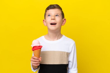Sarı arka planda izole edilmiş kornet dondurmalı beyaz çocuk gülüyor.