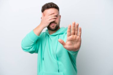 Beyaz arka planda izole edilmiş genç beyaz adam jesti durduruyor ve yüzünü kapatıyor.