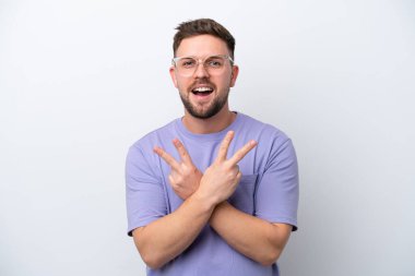 Beyaz arka planda izole edilmiş genç beyaz adam gülümsüyor ve zafer işareti gösteriyor.