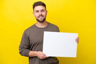 Sarı arka planda izole edilmiş beyaz bir adam elinde mutlu bir ifadeyle boş bir levha tutuyor.