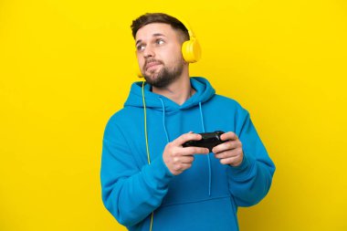 Kafkasyalı genç bir adam, sarı arka planda izole edilmiş bir bilgisayar oyunu kontrolörüyle oynuyor.