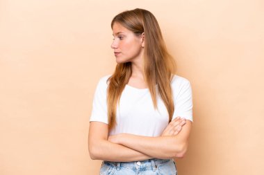 Beyazlı genç bir kadın bej arka planda izole edilmiş, kollarını çapraz tutuyor.
