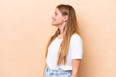 Beyazlı genç bir kadın bej arka planda izole edilmiş. Yan pozisyonda gülüyor.