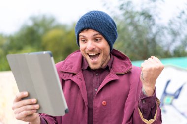 Açık havada elinde tablet tutan genç beyaz bir adam.