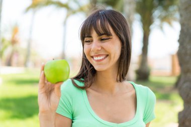 Dışarıda elmalı genç bir kadın, neşeli bir ifadeyle.
